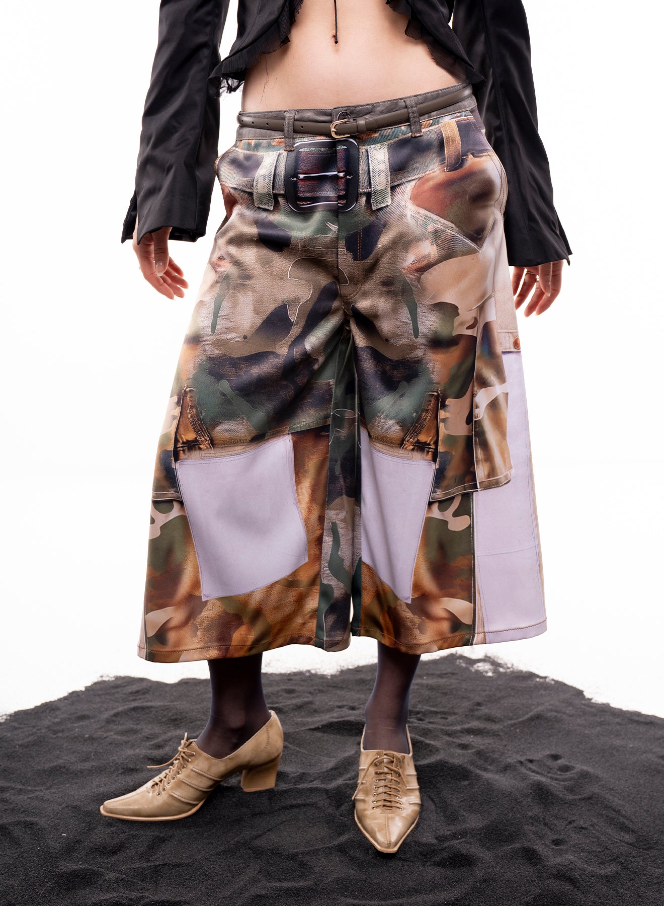 Person wearing a long camouflage skirt with a belt on a black surface.